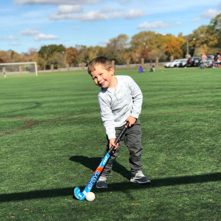 Young boy smiling with a hockey stick and ball on a green field