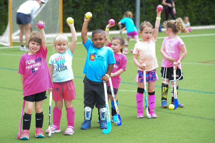 Preschool children celebrating with hockey sticks and balls on a green field